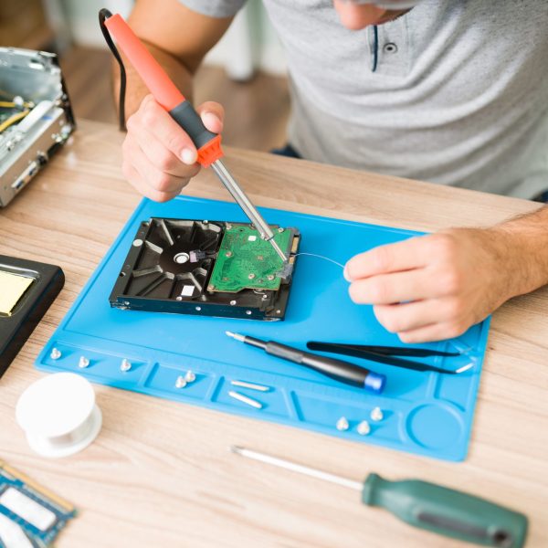 Close up of the technician's hands soldering tin to solder and repair a hard drive on a broken computer CPU